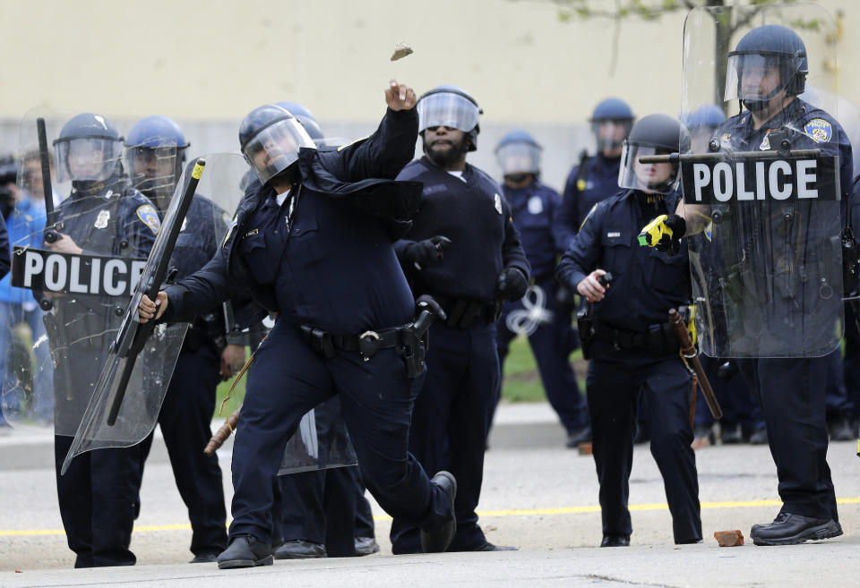 A police officer throws an object at protestors, Monday, April 27, 2015, following the funeral of Freddie Gray in Baltimore. Gray died from spinal injuries about a week after he was arrested and transported in a Baltimore Police Department van. (AP Photo/Patrick Semansky)