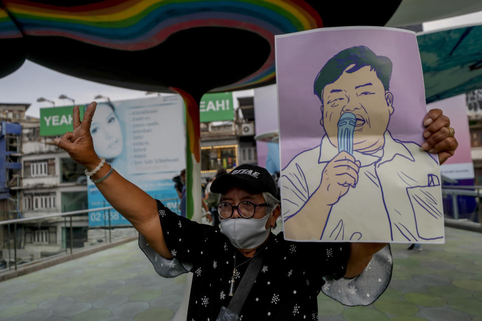 A pro-democracy protester flashes a three-fingered salute and displays an image of protest leader Parit Chiwarak during a protest in Bangkok, Thailand, Wednesday, Feb. 10, 2021. Prosecutors in Thailand on Tuesday charged four prominent pro-democracy activists, including Parit, with sedition and defaming the monarchy for their protest activities. (AP Photo/Sakchai Lalit)