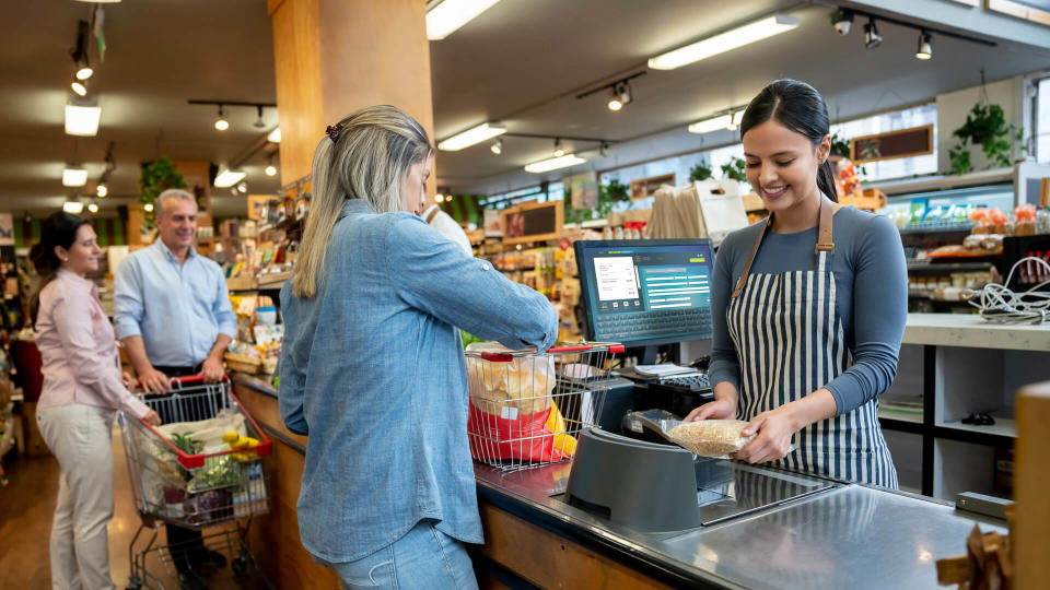 Cheerful employees at supermarket doing checkout for customers  **DESIGN ON SCREEN WAS MADE FROM SCRATCH BY US**.