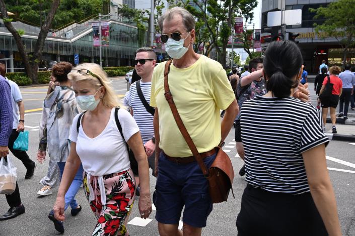 A couple wearing protective facemasks amid fears about the spread of the COVID-19 coronavirus cross a road in Singapore on February 26, 2020. (Photo by ROSLAN RAHMAN / AFP) (Photo by ROSLAN RAHMAN/AFP via Getty Images)
