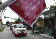 An ambulance carrying the body of a COVID-19 victim drives past a sign that reads "COVID-19 Red Zone," on its way to a cemetery for burial in Bekasi on the outskirts of Jakarta, Indonesia, July 11, 2021. Indonesia surpassed the grim milestone of 100,000 official COVID-19 deaths on Wednesday, Aug. 4, 2021, as the country struggles with its worst pandemic year fueled by the delta variant, with growing concerns that the actual figure could be much higher with people also dying at home. (AP Photo/Achmad Ibrahim)