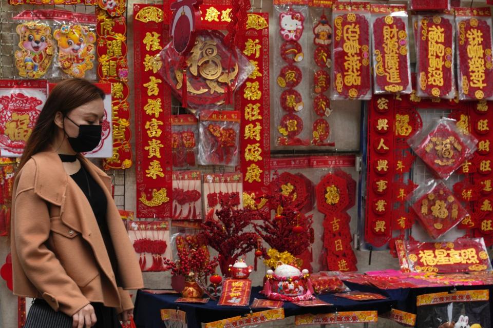 A woman walks past notes containing Chinese New Year calligraphy and decorations are displayed for sale on a street to celebrate the Lunar New Year in Hong Kong, Friday, Jan. 14, 2022. Hong Kong International Airport said Friday that it would ban passengers from over 150 countries and territories from transiting in the city for a month, as it sought to stem the transmission of the highly contagious omicron variant of the coronavirus. (AP Photo/Kin Cheung)