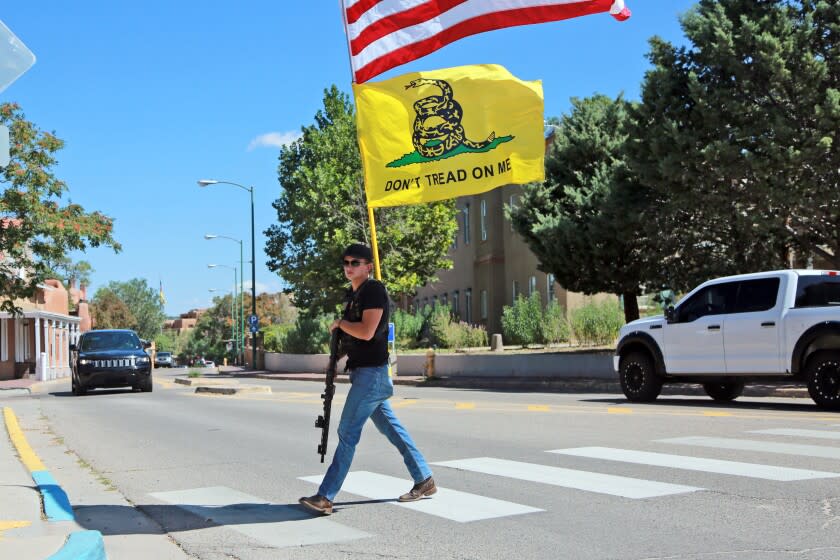 Matthew Vigil crosses a street carrying flags near the state Capitol to protest vaccine and mask mandates on Friday, Aug. 20, 2021, in Santa Fe, N.M.. (AP Photo/Cedar Attanasio)