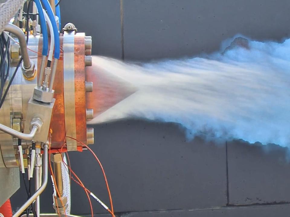 A bright blue flame coming out the back of a jet engine with exposed wiring.