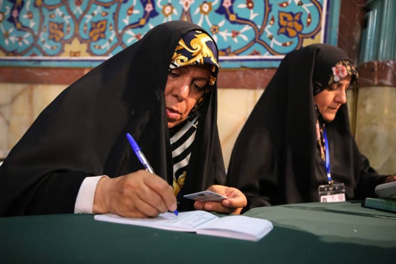 A veiled Iranian female polling station worker checks and registers the Iranian national voter card during the 2024 snap presidential election at Hosseiniyeh Ershad polling station in northern Tehran. Rouzbeh Fouladi/ZUMA Press Wire/dpa