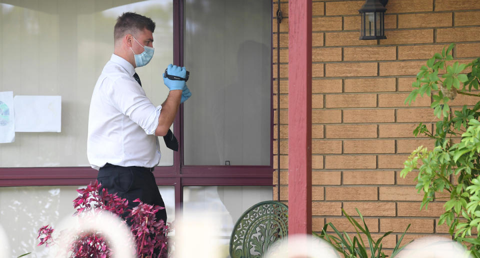 A Victoria Police investigator pictured at the Tullamarine scene. To their left are Claire Perinovic's drawings stuck on the window.