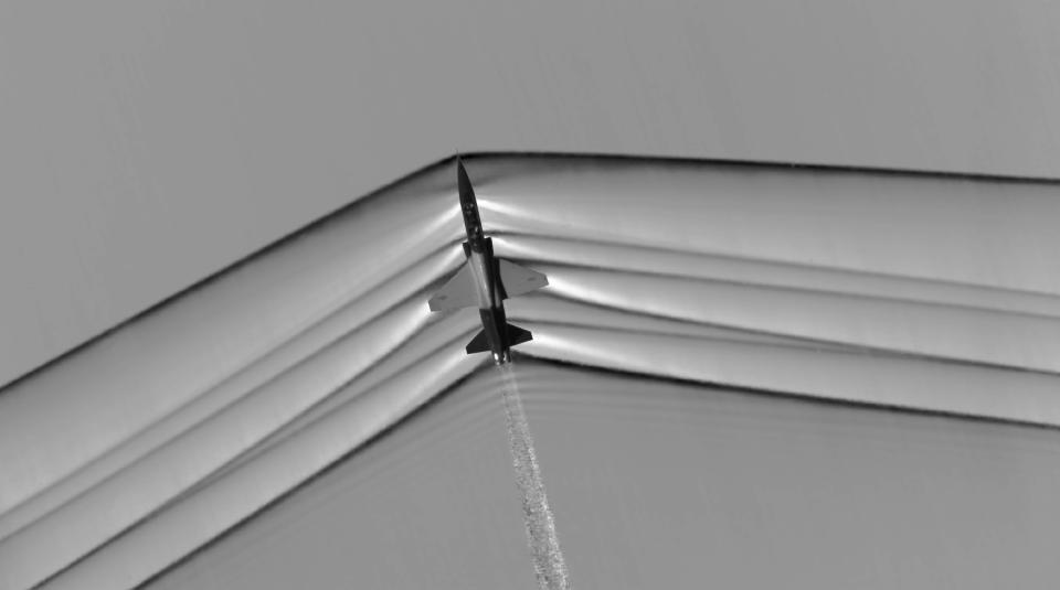 the silhouette of a plane with straight line shockwaves emanating from each side