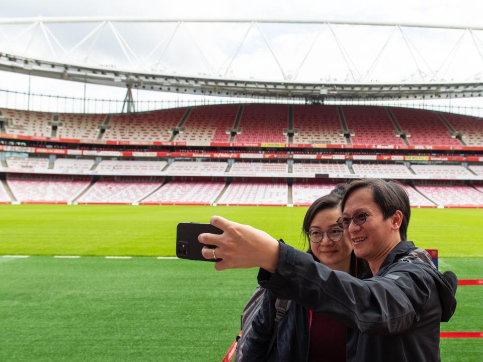 Two people are embrassing as they pose for a selfie in front of the green grass at the Arsenal Emirates stadium, after getting a COVID-19 vaccine on june 25