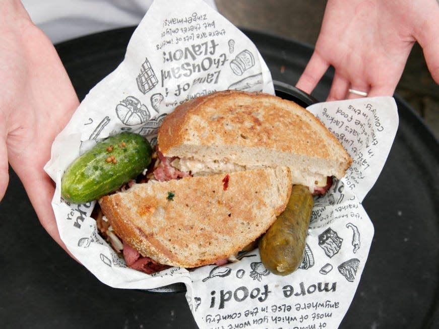 reuben sandwich in newspaper with pickle and pepper