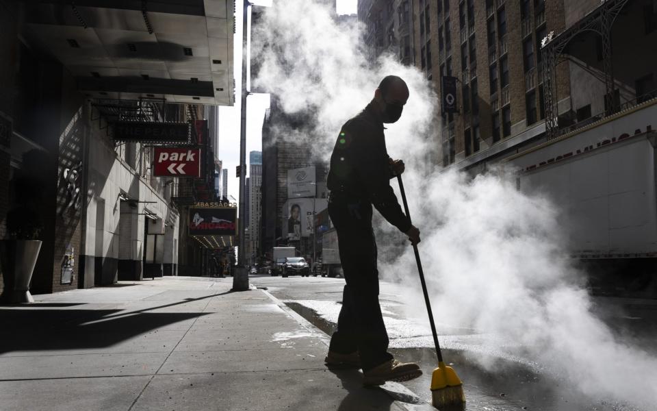 A hotel worker sweeps a quiet street near Times Square where some of the area's Broadway theatres are located in New York - JUSTIN LANE/EPA-EFE/Shutterstock