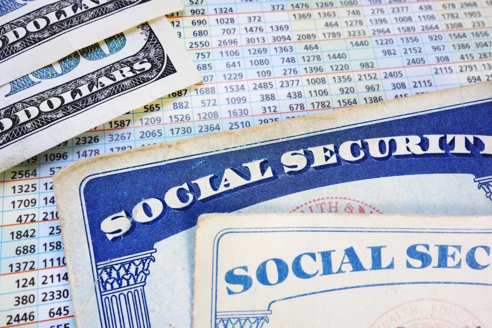 Two Social Security cards and two one-hundred-dollar bills set atop a payment schedule sheet.