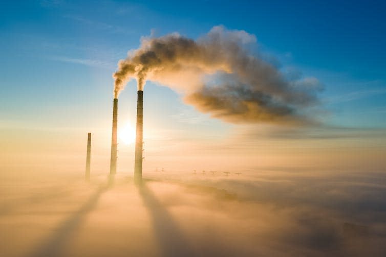 Three smokestacks poking above clouds belching smoke.