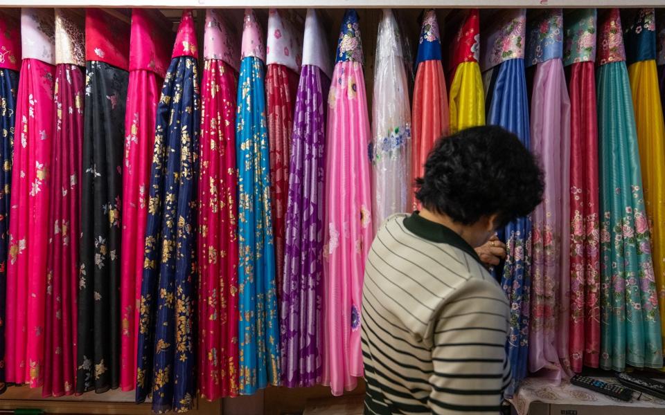 A shop owner who sells traditional Korean clothes looks at all the fabrics in her shop in Dandong - Yan Cong for the Telegraph