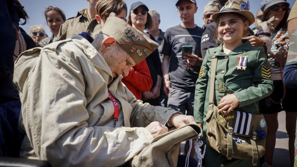 A U.S. veteran signs the bag of a World War II enthusiast during a gathering in preparation of the 79th D-Day anniversary in Sainte-Mere-Eglise Normandy, France, Sunday, June 4, 2023. (Thomas Padilla/AP)