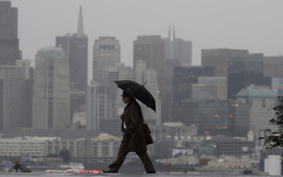 A man carries an umbrella as he crosses the street with the skyline at rear in San Francisco, Friday, Feb. 1, 2019. A powerful storm bearing down on California on Friday was expected to produce heavy rainfall, damaging winds, localized stream flooding and heavy snow in the Sierra Nevada, forecasters said. (AP Photo/Jeff Chiu)