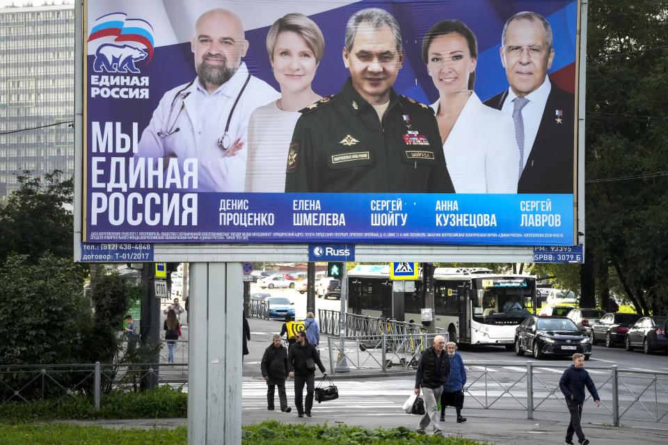 People walk past an election poster in St. Petersburg, Russia, on Saturday, Sept. 11, 2021, ahead of the upcoming election for the State Duma, the lower house of the Russian parliament. The poster, from left, shows Denis Protsenko, head of the educational foundation "Talent and Success"; Yelena Shmeleva; Russian Defense Minister Sergei Shoigu; children's rights ombudsman Anna Kuznetsova; and Russian Foreign Minister Sergey Lavrov, candidates of the pro-Kremlin United Russia Party during the campaign. (AP Photo/Dmitri Lovetsky)