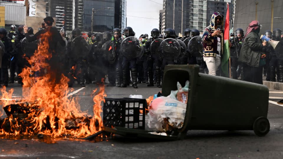 Fire burns ahead of a Victoria Police riot squad line during a rally against the Land Forces International Land Defense Exposition in Melbourne, Australia September 11, 2024. - Joel Carrett/AAP/Reuters