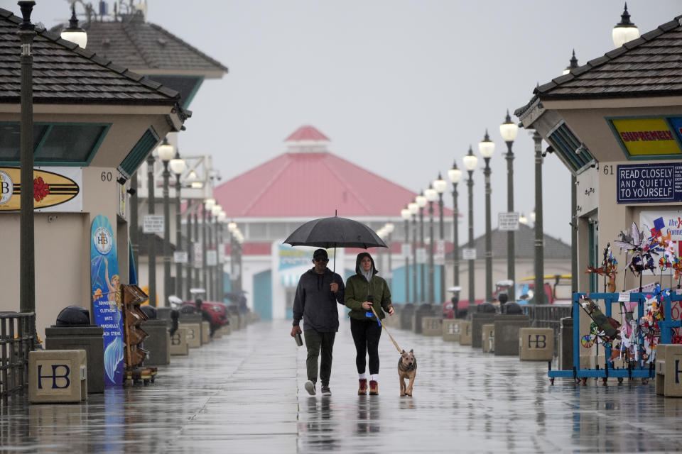 A couple walk in the rain with their dog along the Huntington Beach Pier on Tuesday, Feb. 6, 2024, in Huntington Beach, Calif. (AP Photo/Marcio Jose Sanchez)