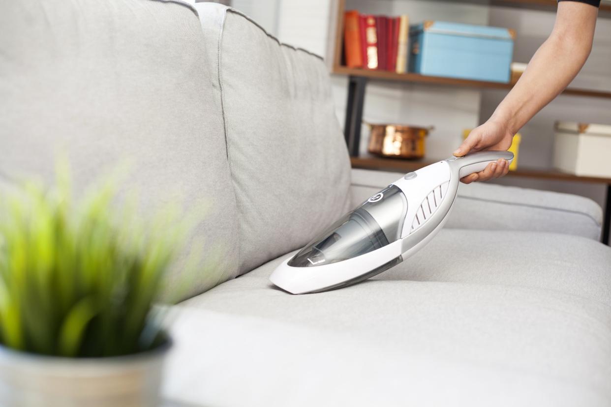 Vacuuming the couch with a hand-held vacuum. 