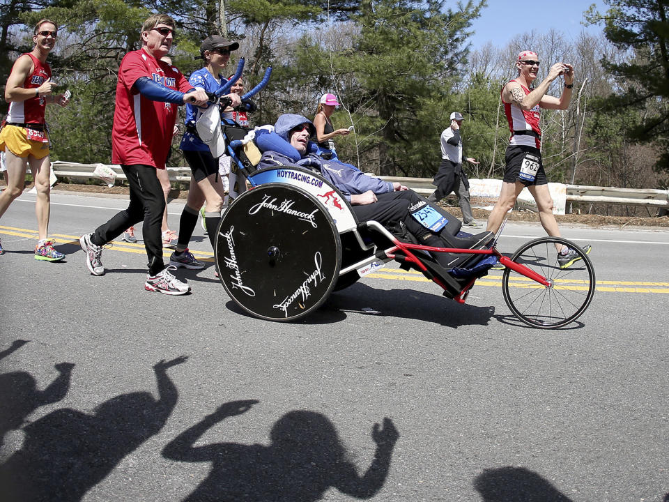 FILE - In this April 21, 2014, file photo, Dick Hoyt, left, pushes his son Rick during the Boston Marathon together as they pass through Wellesley, Mass. Dick Hoyt, who last competed with his son in the Boston Marathon in 2014, has died, the Boston Athletic Association announced Wednesday, March 17, 2021. He was 80. (AP Photo/Mary Schwalm, File)