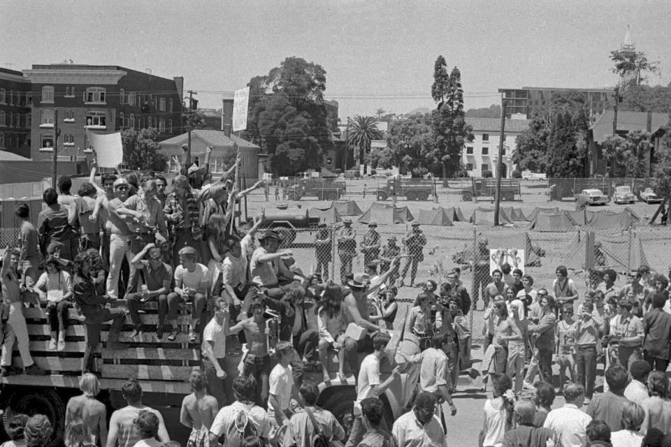 FILE - National Guardsmen stand guard on the other side of a steel mesh fence erected by University of California officials around People's Park at Berkeley, Calif., while some of the thousands who marched in protest pass by on May 15, 1969. The three-acre site's colorful history, forged from University of California, Berkeley's seizure of the land in 1968, has been thrust back into the spotlight by the school's renewed effort to pave over People's Park as part of a $312 million project that includes sorely needed housing for about 1,000 students. (AP Photo, File)