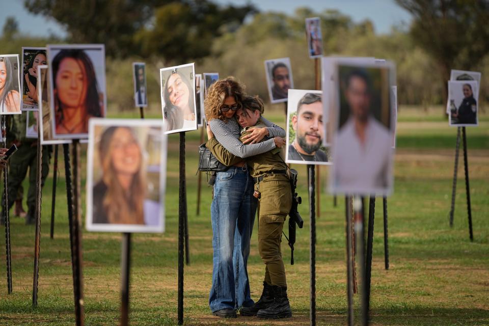 Israelis embrace next to photos of people killed and taken captive by Hamas militants during their violent rampage through the Nova music festival in southern Israel, which are displayed at the site of the event, as Israeli DJs spun music, to commemorate the October 7 massacre, near kibbutz Re'im, Tuesday, Nov. 28, 2023.