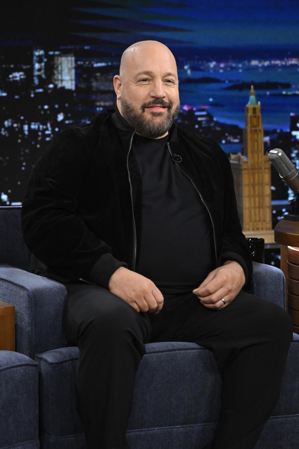 Kevin James in dark velvet jacket seated on a talk show couch