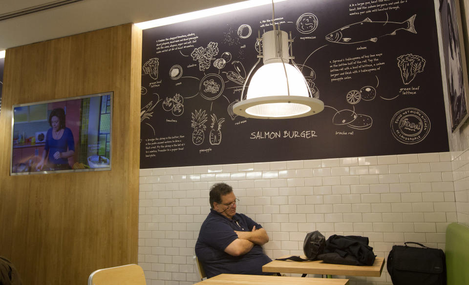 In this Wednesday, Nov. 14, 2012 photo, an airline passenger rests in the Food Network Kitchen, as Rachael Ray appears on a TV in the cafe at the Fort Lauderdale-Hollywood International Airport, in Fort Lauderdale, Fla. Dining-on-the-go is soaring at the airport where travelers can dine at a restaurant inspired by a test kitchen. (AP Photo/J Pat Carter)