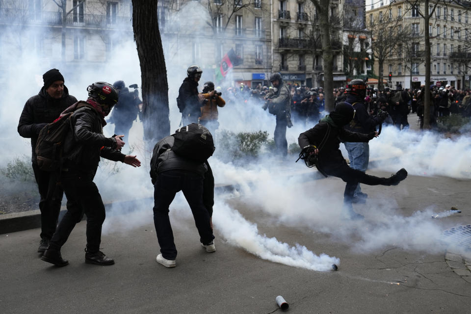 Youths kick tear gas during a demonstration, Tuesday, March 7, 2023 in Paris. Demonstrators were marching across France on Tuesday in a new round of protests and strikes against the government's plan to raise the retirement age to 64, in what unions hope to be their biggest show of force against the proposal. (AP Photo/Lewis Joly)