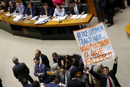 A supporter of the Brazilian President Michel Temer holds a banner at the lower chamber of Brazil's Congress before a vote session on whether the Congress allows charges against President Michel Temer to be sent to the Supreme Court for trial, in Brasilia, Brazil October 25, 2017. The banner reads: "Let the Man work, go look for whatever to do!!" REUTERS/Adriano Machado