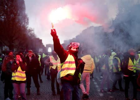 A protester wearing yellow vest, a symbol of a French drivers' protest against higher fuel prices, burns flare on the the Champs-Elysee in Paris, France, November 24, 2018. REUTERS/Benoit Tessier
