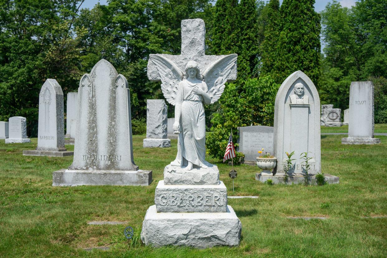 Hope Cemetery, Barre, Vermont, several large headstones and statues in barre grey granite surrounded by grass with trees in the background on a sunny summer day