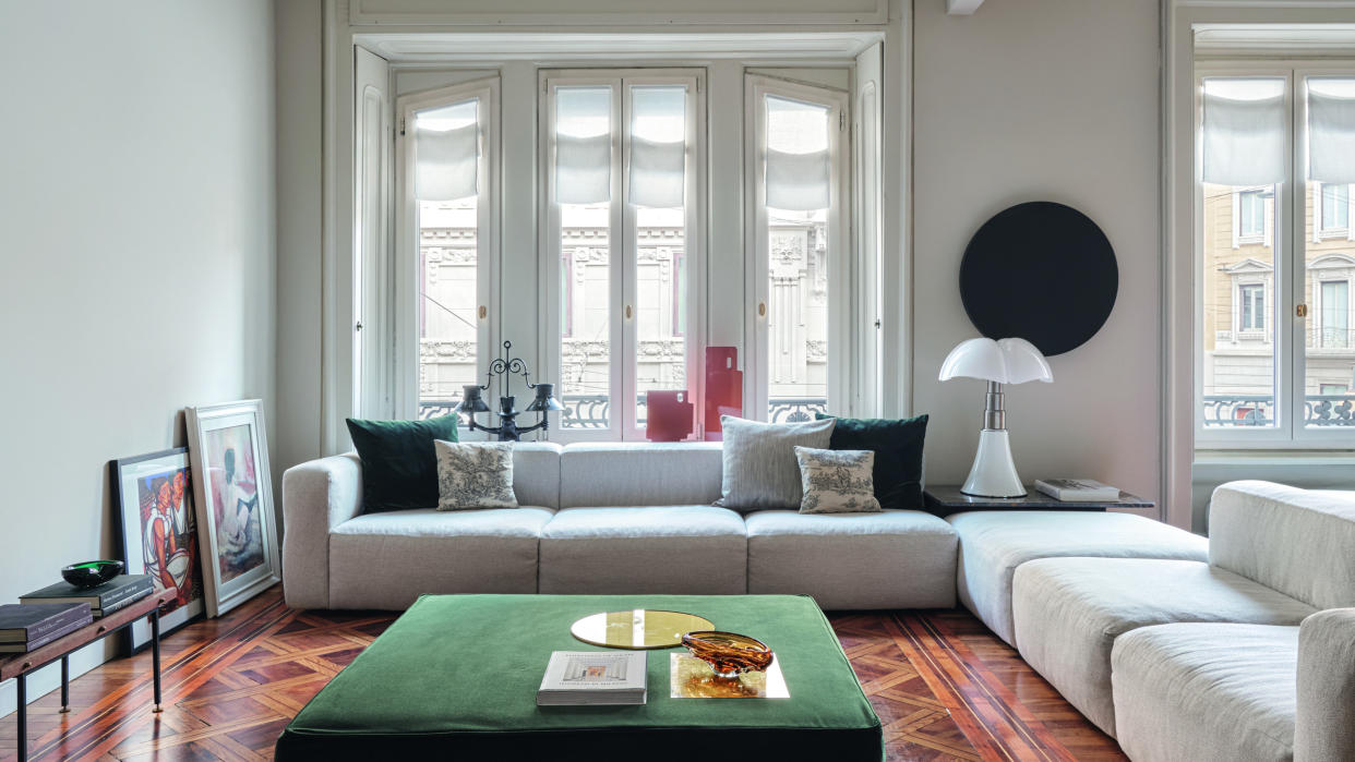  White living room with polished wood floor, white modular corner sofa and green velvet upholstered coffee table. 