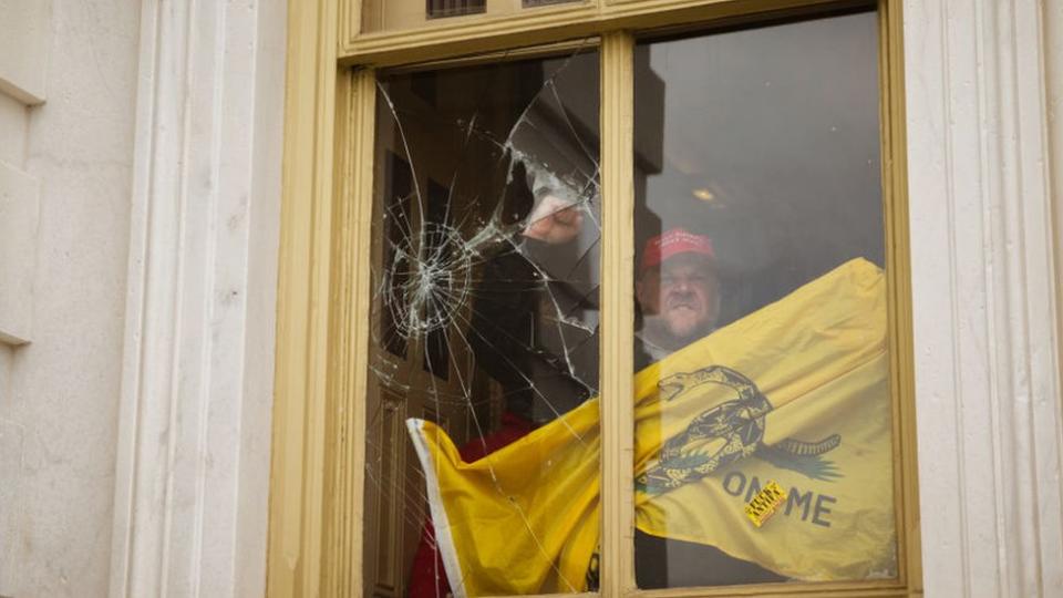 Uno de los invasores del Capitolio alza el puño frente a una ventana rota por causa de los destrozos en el edificio.