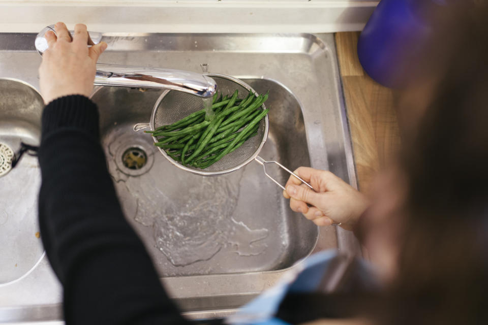 A close up of green beans being washed with water in a kitchen sink. 