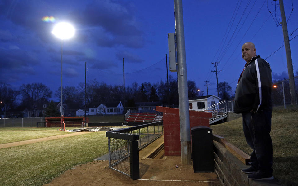 Activities director Dave Boie, right, looks out over the lit baseball field at Richfield High School Wednesday night, April 8, 2020 in Richfield, Minn. Seeking to brighten spirits amid the virus outbreak, the symbolic act of turning on the lights became a movement — fueled by social media with the hashtag #BeTheLight — across the country. (AP Photo/Jim Mone)