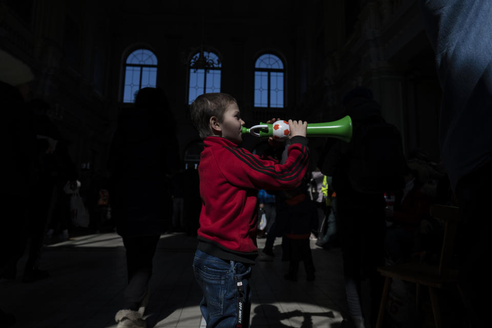 A boy plays with a toy horn as he and his family who fled the war in Ukraine wait at the train station in Przemysl, southeastern Poland, on Monday, March 14, 2022. (AP Photo/Petros Giannakouris)