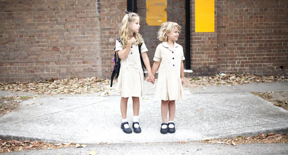 Two little girls in school uniforms wait to cross the road. Source: Getty Images