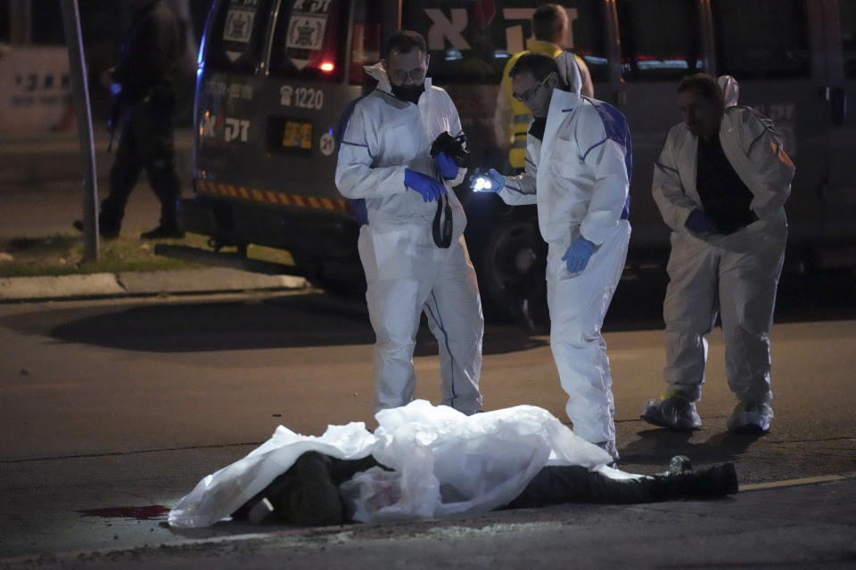 Israeli police stand next to a body of a victim as they inspect the scene of a shooting attack In Hadera, Israel, Sunday, March 27, 2022. A pair of gunmen killed two people and wounded four others in a shooting spree in central Israel before they were killed by police, according to police and medical officials. The identity of the gunmen was not immediately known, but police called them "terrorists," the term usually used for Arab assailants. (AP Photo/Ariel Schalit)
