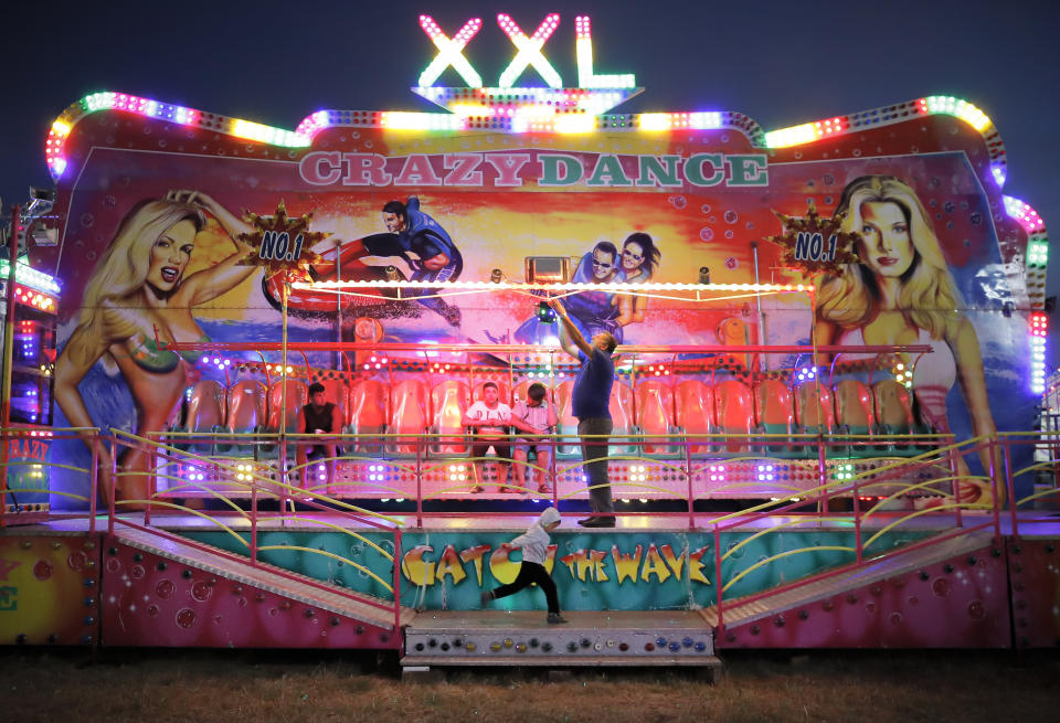 In this picture taken Thursday, Sept. 12, 2019, a small child runs by as a man adjusts a lights of a ride at an autumn fair in Titu, southern Romania. Romania's autumn fairs are a loud and colorful reminder that summer has come to an end and, for many families in poorer areas of the country, one of the few affordable public entertainment events of the year. (AP Photo/Vadim Ghirda)