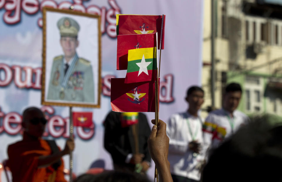 A supporter holds flags of Myanmar National and military while a portrait of Senior Gen. Min Aung Hlaing displays in the background during a pro-military rally Sunday, Oct. 14, 2018, in front of city hall in Yangon, Myanmar. Several thousand pro-military and nationalist demonstrators marched through Yangon on Sunday voicing their support for Myanmar's armed forces and government while condemning foreign involvement in the country's affairs. (AP Photo/Thein Zaw)