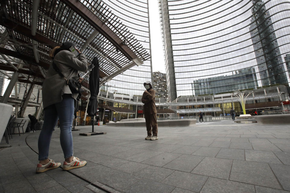 A woman wearing a protective mask stands at the Porta Nuova business district in Milan, Italy, Thursday, Feb. 27, 2020. In Europe, an expanding cluster in northern Italy is eyed as a source for transmissions of the COVID-19 disease. (AP Photo/Luca Bruno)