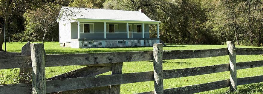 Main farmhouse at Richmond Hamilton Farm – White Farmhouse with long covered front porch in large green field – Photo Courtesy: New River Gorge National Park and Preserve