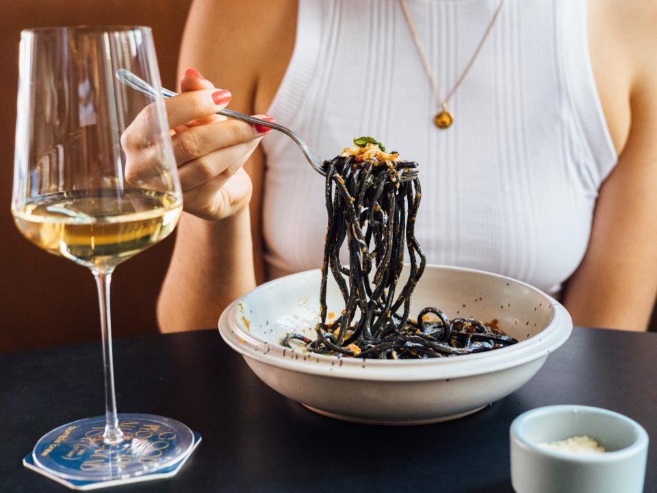 A person eating a plate of chitarra nero, crab, and Japanese mint with a glass of white wine next to them.