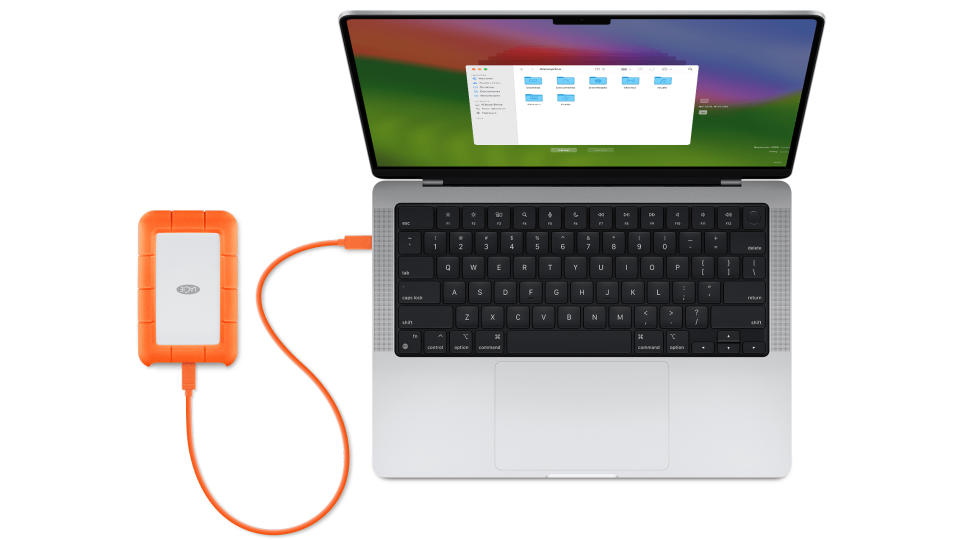 Vista aérea de um MacBook Pro aberto com um disco rígido externo laranja conectado (esquerda).