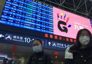 Passengers wearing masks walk under a train information board at the Beijing West Railway Station, in Beijing