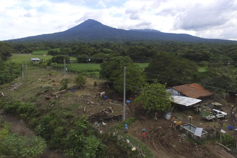 A family works on their farm littered with trunks of trees that were felled by last year's October landslide, backdropped by the San Salvador volcano in Los Angelitos, El Salvador, Wednesday, July 28, 2021. The 2020 Atlantic hurricane season, one of the worst ever for Central America, wiped out homes and crops and displaced more than half a million people. (AP Photo/Salvador Melendez)