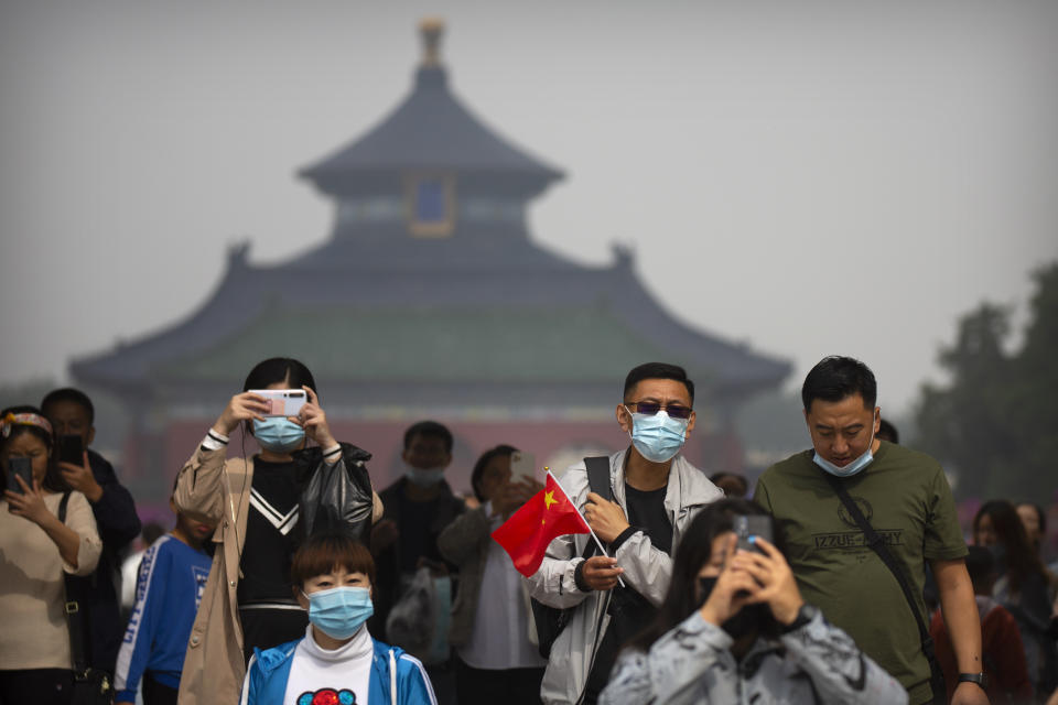 A man wearing a face mask to protect against the coronavirus holds a Chinese flag as he visits the Temple of Heaven in Beijing, Thursday, Oct. 1, 2020. Millions of Chinese tourists usually would use their week-long National Day holidays to travel abroad. This year, travel restrictions due to the coronavirus pandemic mean that some 600 million tourists - about 40% of the population - will travel within China during the holiday that began Thursday, according to Ctrip, China's largest online travel agency (AP Photo/Mark Schiefelbein)