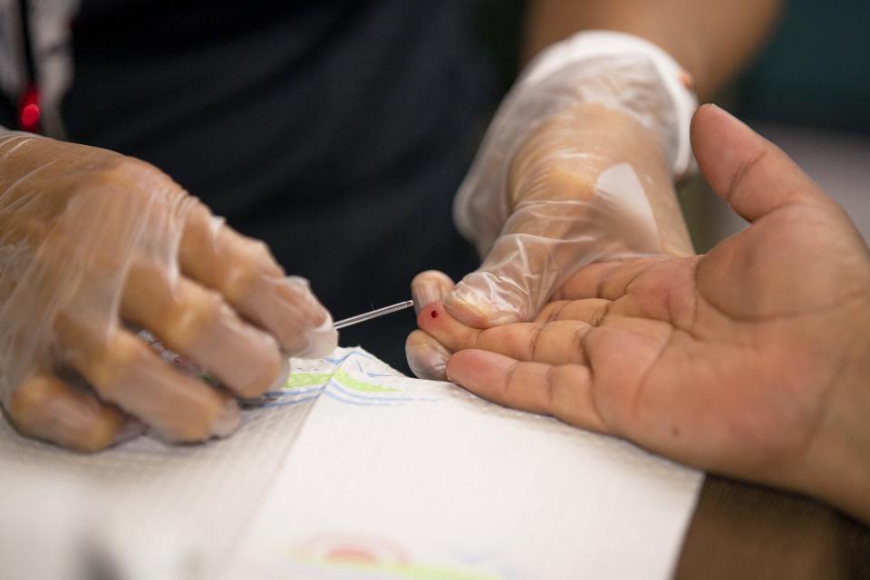 A community health worker pricks the finger of a patient to assess blood sugar levels.