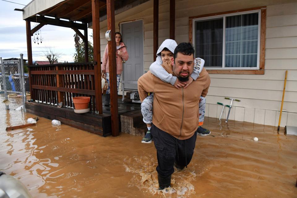 Ryan Orosco, of Brentwood, carries his son Johnny, 7, on his back while his wife Amanda Orosco waits at the front porch to be rescued from their flooded home on Bixler Road in Brentwood, Calif., on Monday, Jan. 16, 2023